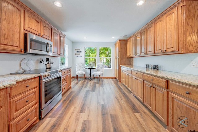 kitchen with stainless steel appliances, light wood-type flooring, and light stone countertops