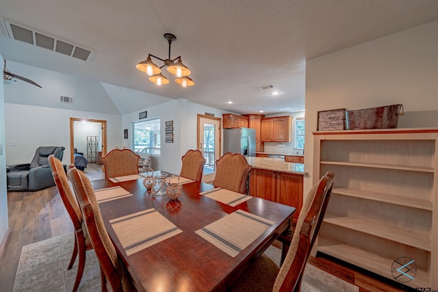 dining space featuring light hardwood / wood-style floors, an inviting chandelier, lofted ceiling, and a textured ceiling