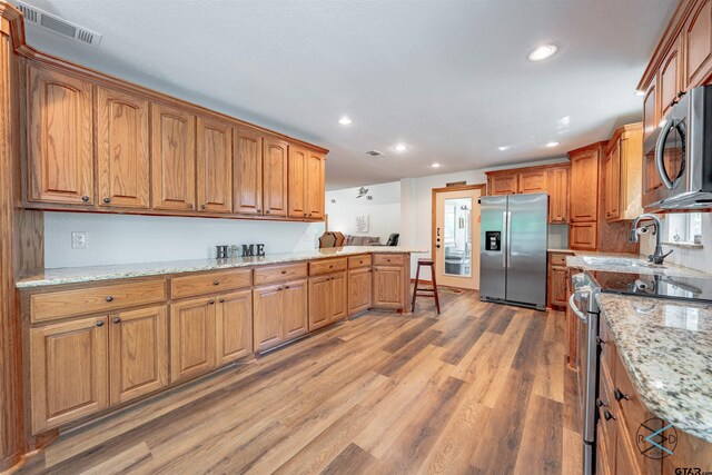 kitchen with stainless steel appliances, sink, light stone counters, a kitchen breakfast bar, and hardwood / wood-style flooring