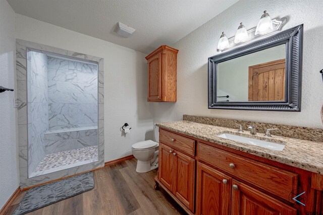 bathroom featuring toilet, hardwood / wood-style flooring, a textured ceiling, a shower, and vanity