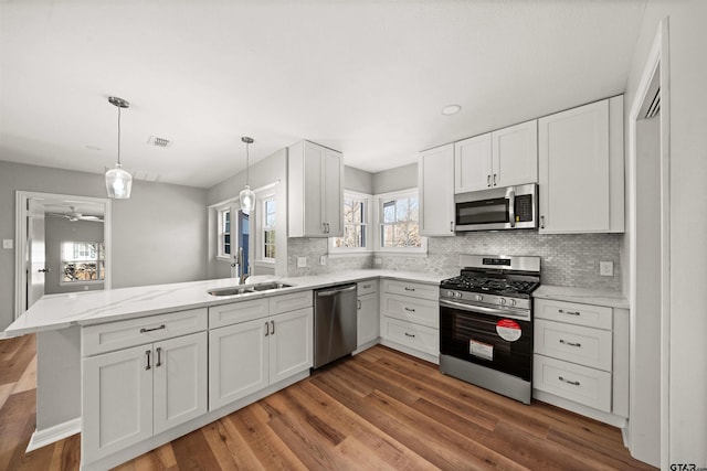 kitchen featuring white cabinetry, decorative backsplash, a sink, stainless steel appliances, and a peninsula