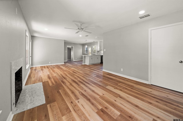 unfurnished living room featuring ceiling fan, light wood finished floors, baseboards, visible vents, and a fireplace with flush hearth