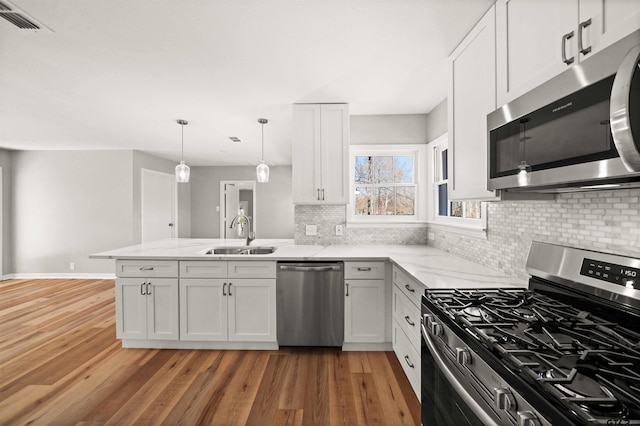 kitchen with decorative backsplash, light wood-style floors, appliances with stainless steel finishes, a sink, and a peninsula