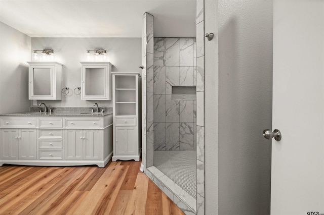 bathroom featuring a marble finish shower, a sink, double vanity, and wood finished floors