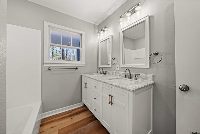 bathroom featuring baseboards, wood finished floors, crown molding, and a sink