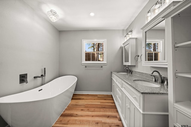 full bath with a sink, a freestanding bath, wood finished floors, and baseboards