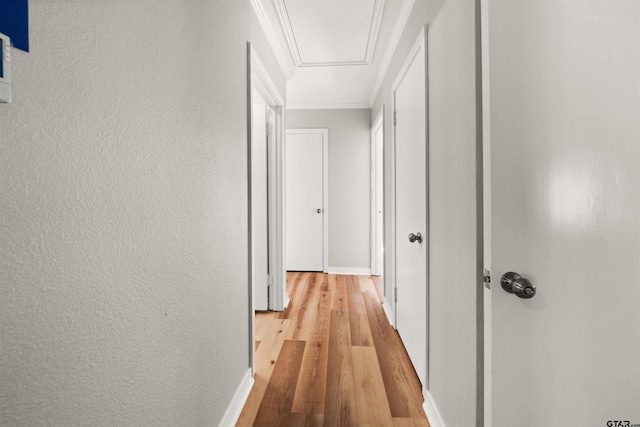 corridor featuring attic access, light wood finished floors, ornamental molding, and baseboards