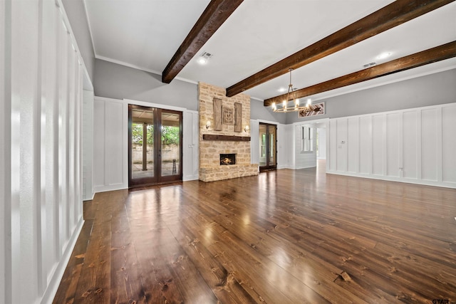 unfurnished living room with dark wood finished floors, beamed ceiling, a stone fireplace, french doors, and an inviting chandelier