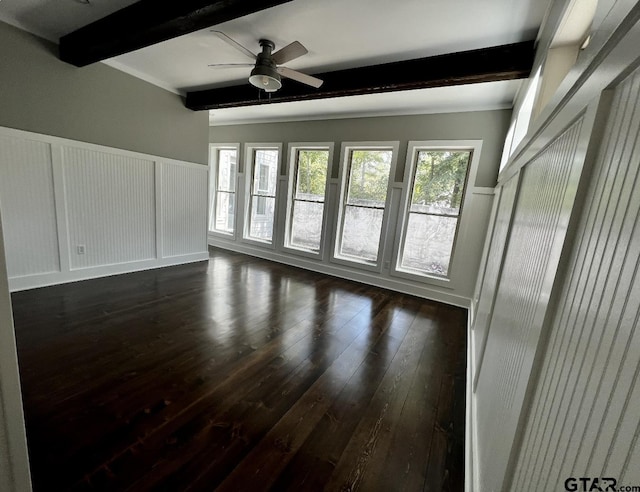 unfurnished living room featuring beamed ceiling, wainscoting, a decorative wall, and dark wood-style flooring