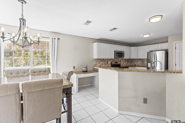 kitchen featuring light stone countertops, stainless steel appliances, white cabinetry, backsplash, and a notable chandelier
