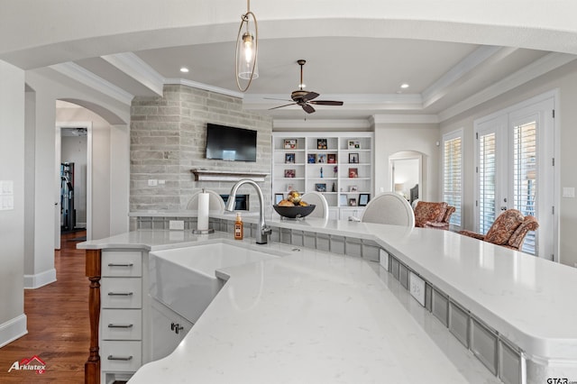 kitchen featuring sink, light stone counters, dark hardwood / wood-style flooring, decorative light fixtures, and a raised ceiling