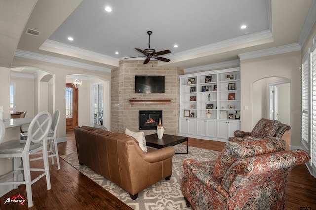 living room featuring ceiling fan, a large fireplace, a tray ceiling, and hardwood / wood-style floors