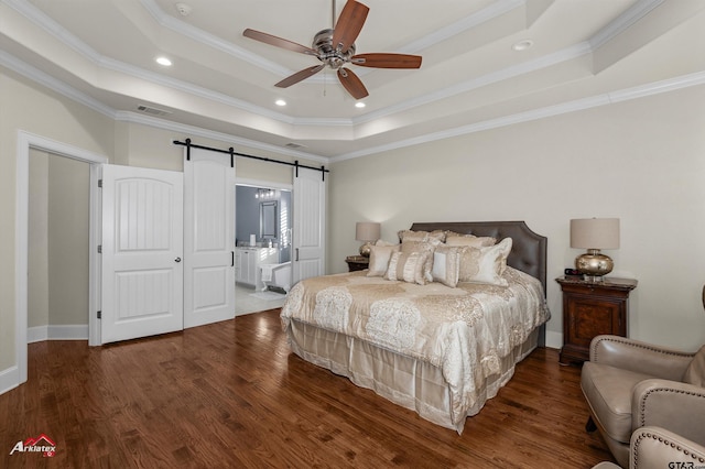 bedroom featuring ensuite bathroom, crown molding, a tray ceiling, a barn door, and hardwood / wood-style floors