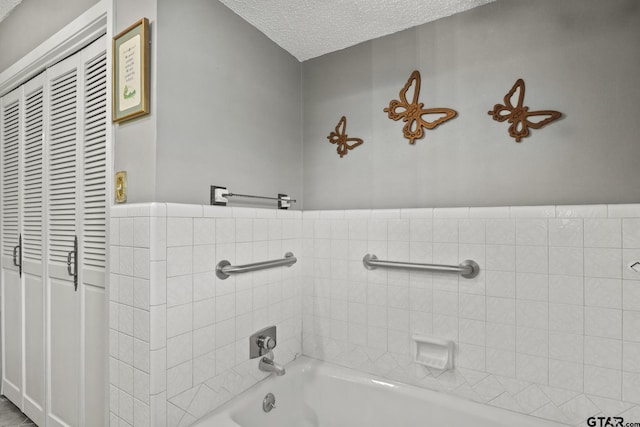 bathroom with a washtub, a textured ceiling, and tile walls