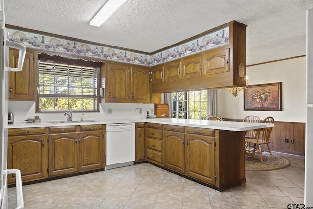 kitchen with dishwasher, sink, kitchen peninsula, wood walls, and a textured ceiling