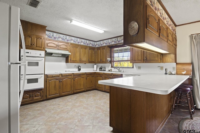 kitchen featuring kitchen peninsula, ornamental molding, white appliances, a textured ceiling, and a breakfast bar area