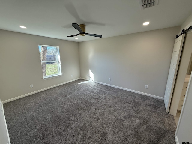 spare room with a barn door, ceiling fan, and dark colored carpet