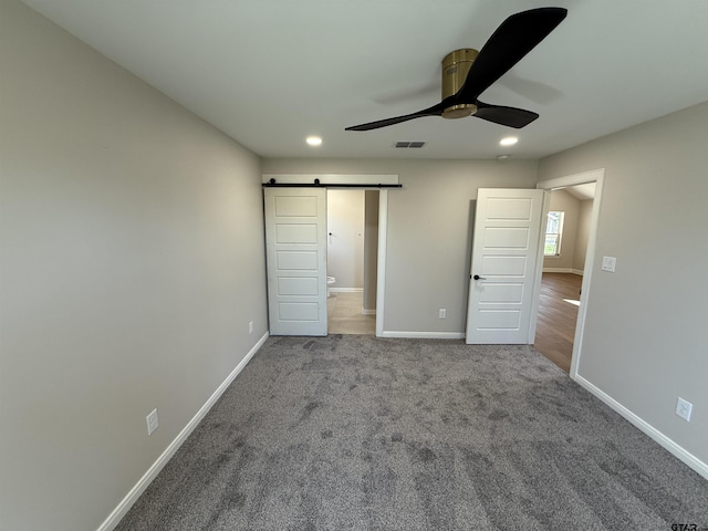 unfurnished bedroom with carpet, ceiling fan, and a barn door