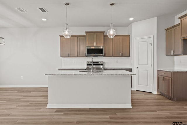 kitchen with a center island with sink, light stone counters, stainless steel appliances, and hardwood / wood-style floors