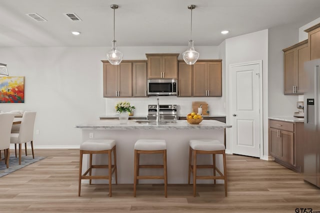 kitchen with sink, a kitchen island with sink, stainless steel appliances, decorative backsplash, and light wood-type flooring