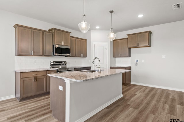 kitchen featuring a kitchen island with sink, sink, hardwood / wood-style flooring, light stone countertops, and stainless steel appliances