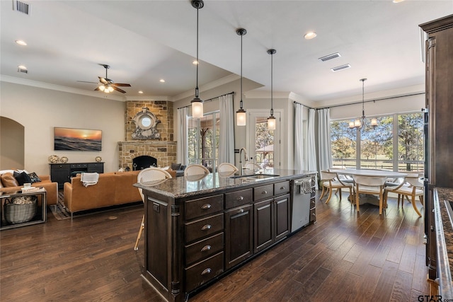 kitchen featuring a stone fireplace, dishwasher, dark brown cabinetry, sink, and a kitchen island with sink