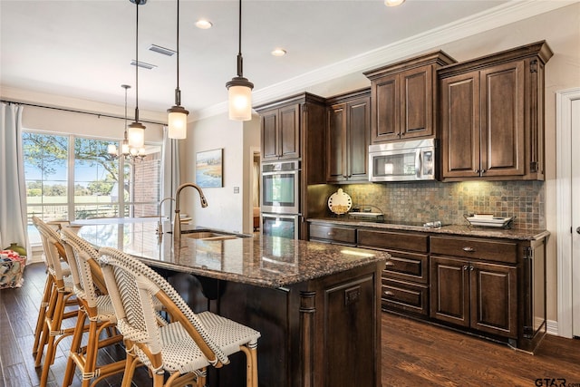 kitchen featuring stainless steel appliances, dark hardwood / wood-style flooring, pendant lighting, sink, and a kitchen island with sink