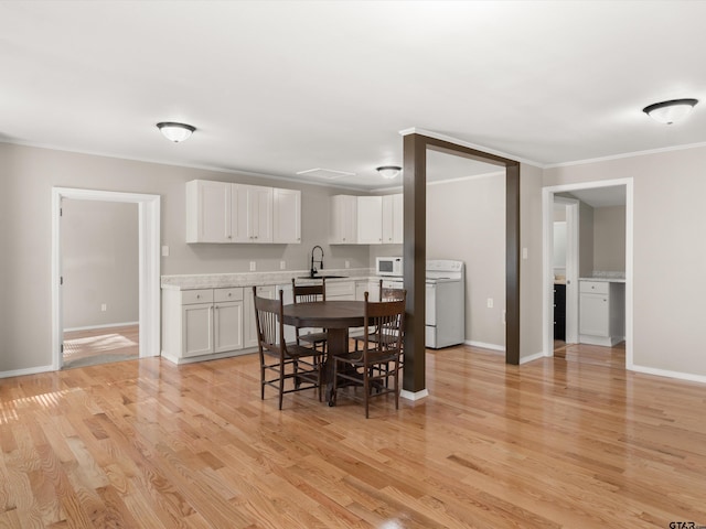 dining area featuring washer / dryer, light hardwood / wood-style flooring, ornamental molding, and sink