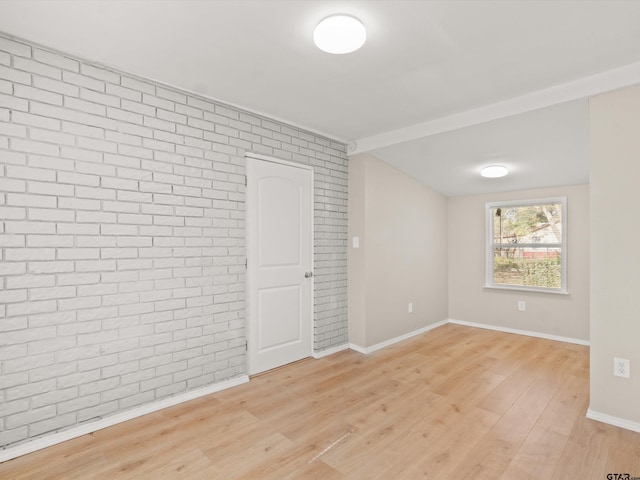 spare room featuring brick wall and light hardwood / wood-style flooring