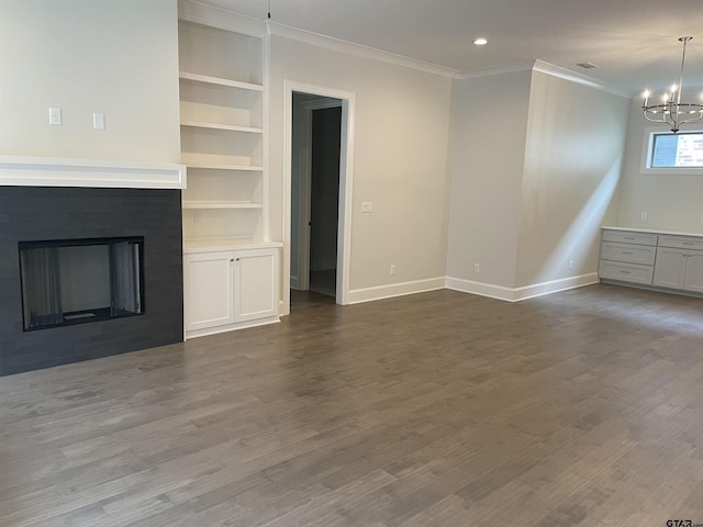 unfurnished living room featuring crown molding, dark hardwood / wood-style floors, a chandelier, and built in shelves