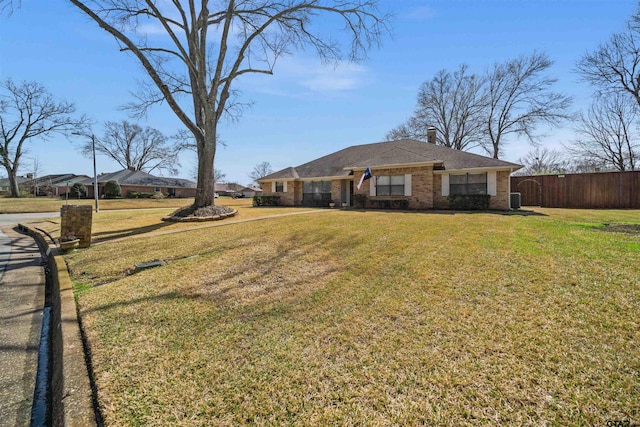 view of front of house featuring a front yard, fence, brick siding, and a chimney