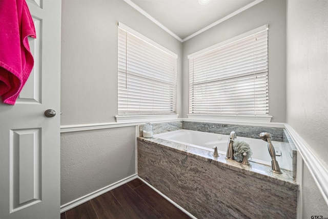 bathroom with a garden tub, ornamental molding, wood finished floors, baseboards, and a textured wall