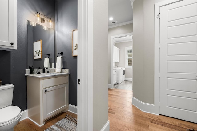 bathroom featuring hardwood / wood-style floors, washer / clothes dryer, ornamental molding, vanity, and toilet