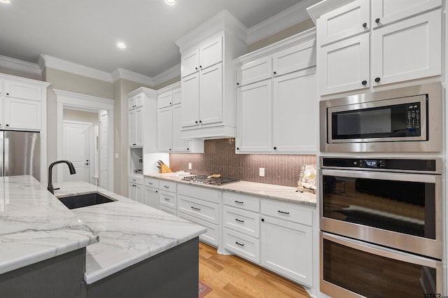 kitchen with white cabinetry, sink, ornamental molding, light stone counters, and stainless steel appliances