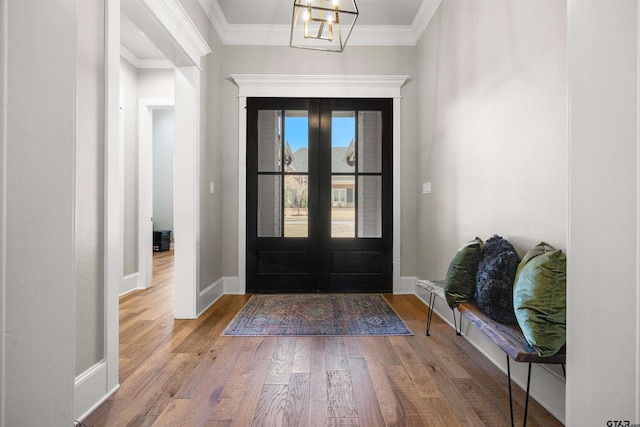 entryway with hardwood / wood-style floors, crown molding, a notable chandelier, and french doors