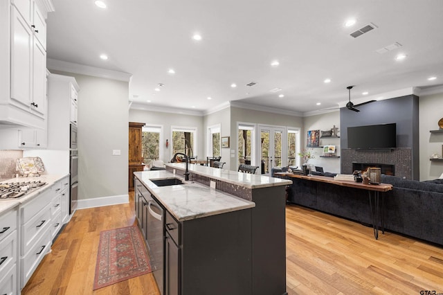 kitchen with white cabinetry, sink, light stone countertops, and a center island with sink