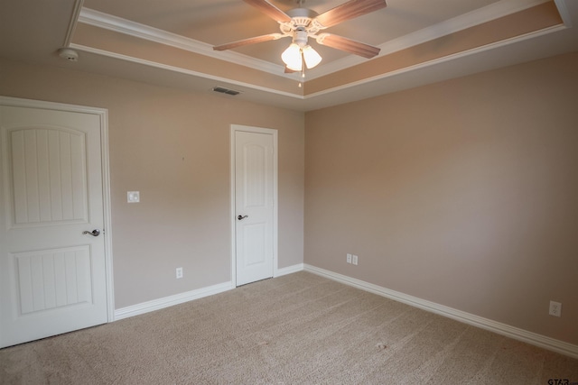carpeted spare room with ceiling fan, attic access, crown molding, a raised ceiling, and baseboards