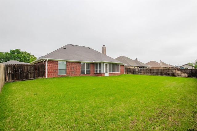 rear view of property with a fenced backyard, a chimney, a yard, and brick siding
