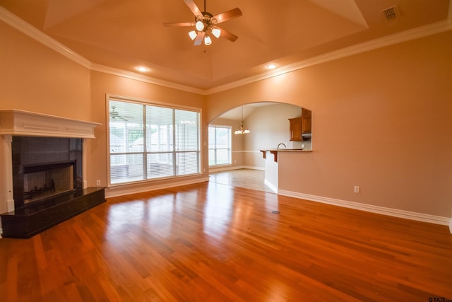 unfurnished living room featuring a fireplace, arched walkways, ceiling fan with notable chandelier, baseboards, and wood finished floors