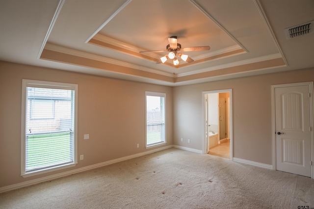 unfurnished bedroom with visible vents, a tray ceiling, multiple windows, and light colored carpet