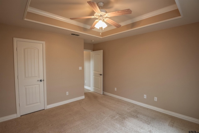 unfurnished bedroom with ornamental molding, light carpet, a tray ceiling, and visible vents
