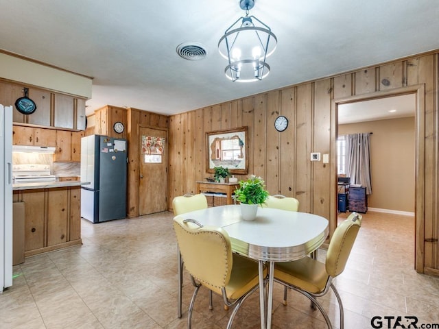 dining space with an inviting chandelier and wooden walls