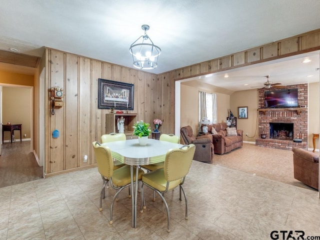 dining room featuring wooden walls, a fireplace, and ceiling fan with notable chandelier