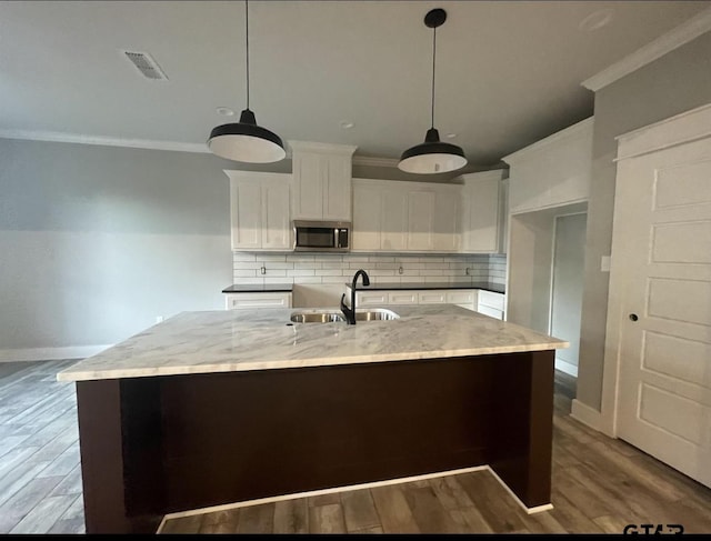 kitchen with white cabinetry, a center island with sink, stainless steel microwave, and a sink