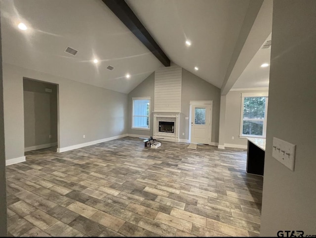 unfurnished living room with a fireplace, beamed ceiling, plenty of natural light, and wood finished floors