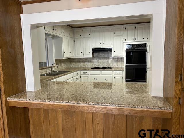kitchen with dobule oven black, a sink, a peninsula, stone counters, and under cabinet range hood