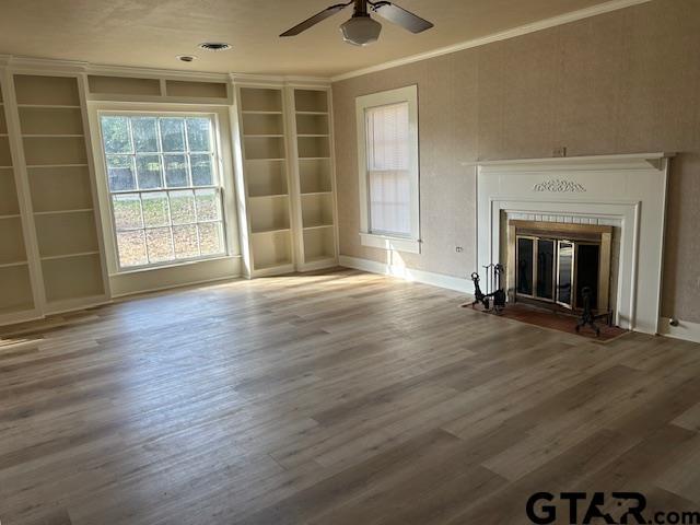 unfurnished living room featuring crown molding, a fireplace with flush hearth, a ceiling fan, and wood finished floors