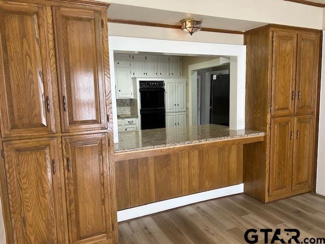 kitchen with dobule oven black, stone counters, and brown cabinets