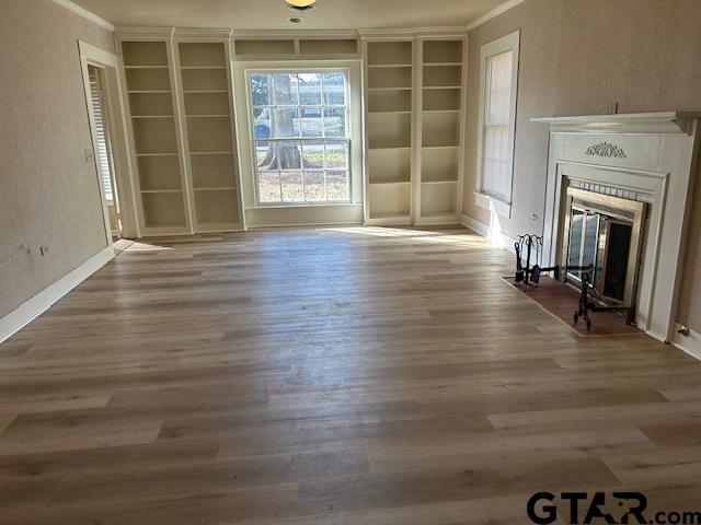 unfurnished living room with a fireplace with flush hearth, built in features, wood finished floors, baseboards, and ornamental molding