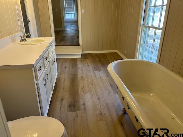 bathroom featuring wood finished floors, vanity, baseboards, toilet, and a soaking tub